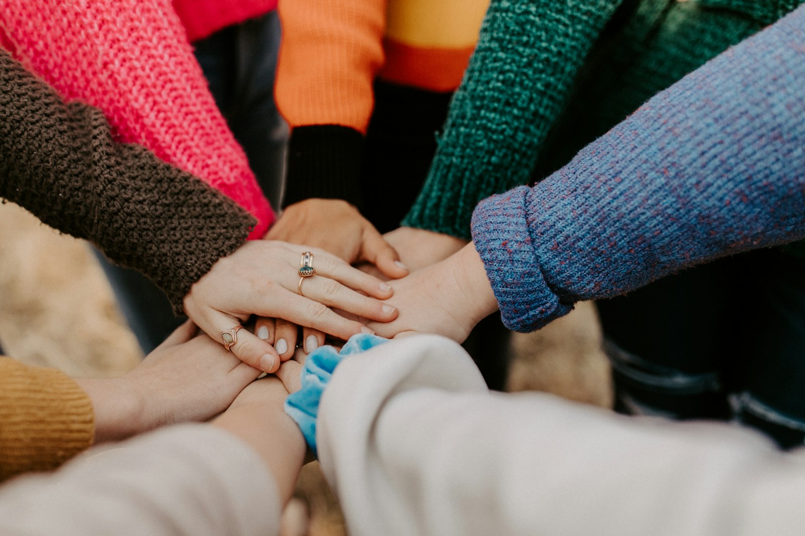 Hands of people in colourful knitwear joined together in a circle